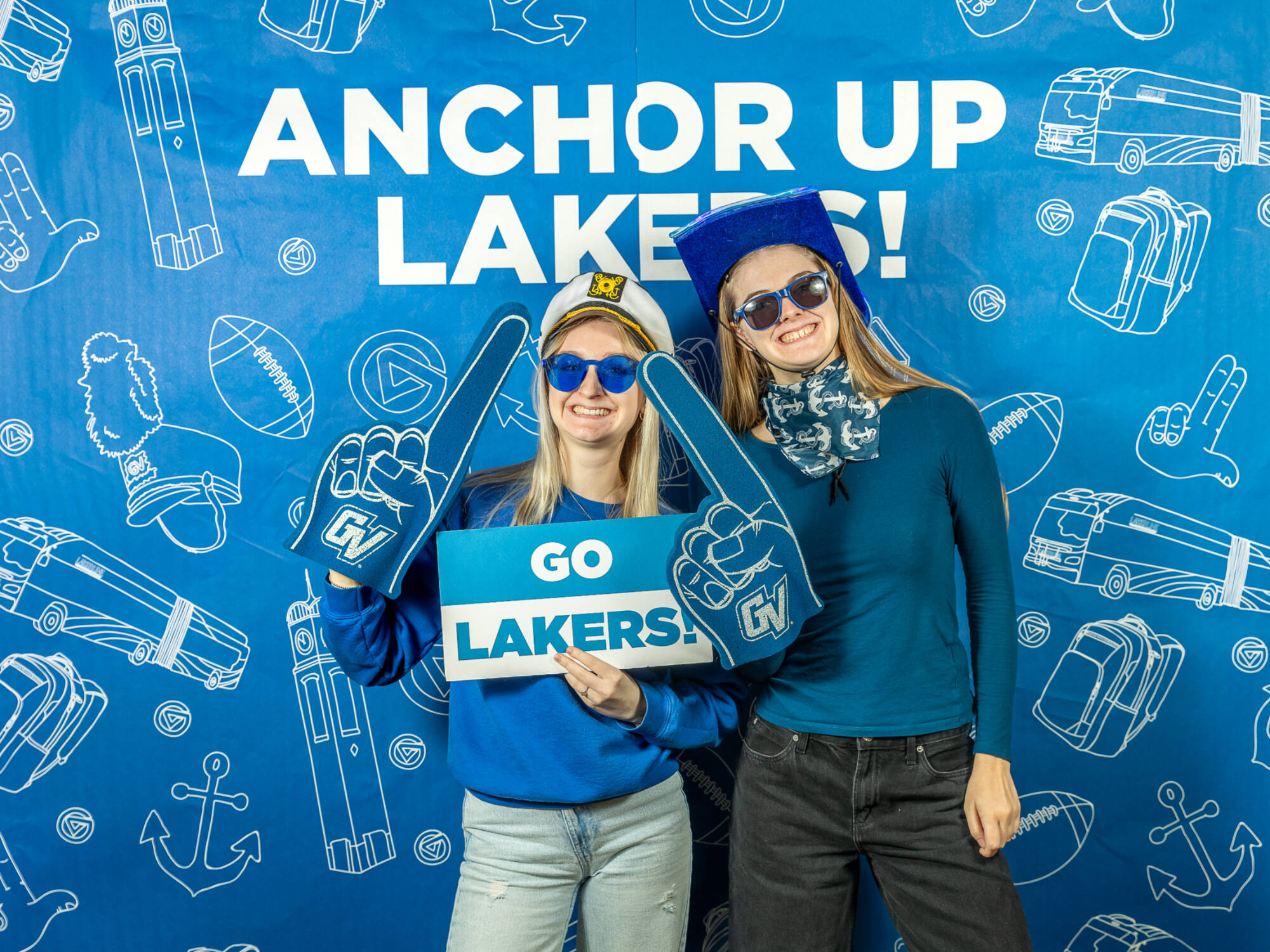 Two individuals holding gvsu foam fingers, with a Go Lakers! sign and wearing hats
